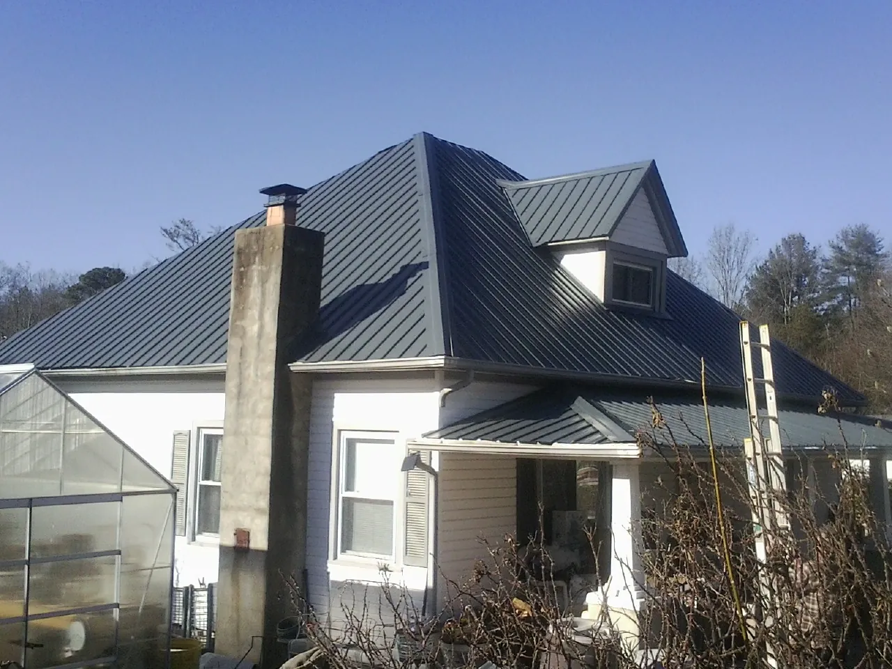 Dark blue standing seam metal roof on a white farmhouse with dormer — Slate & Tile Roof Repair by Roofing Brothers in Newfield