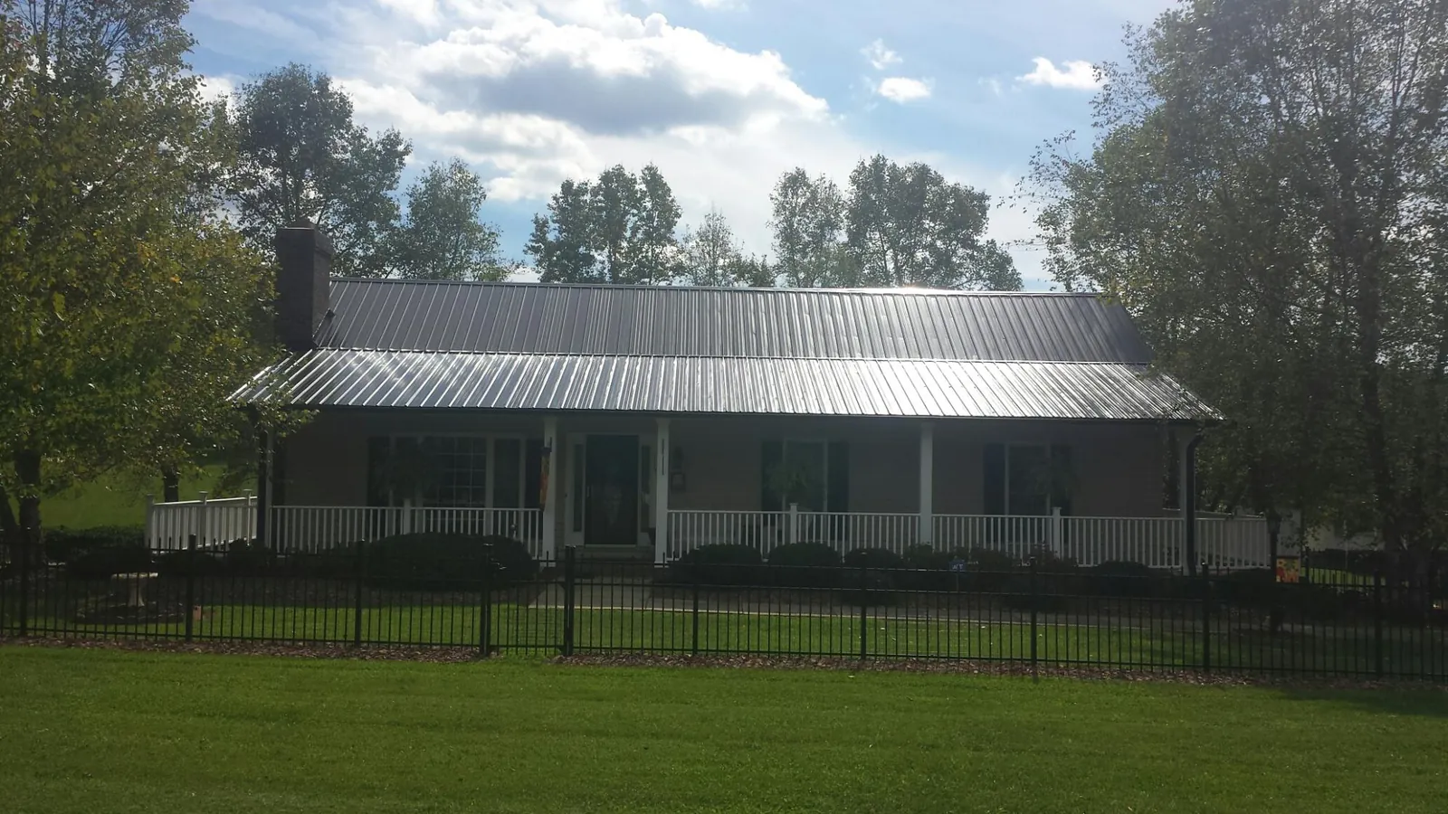 Gray metal roof on a brick ranch with a full width front porch — Gutter Guard Installation work by our crew in Newfield